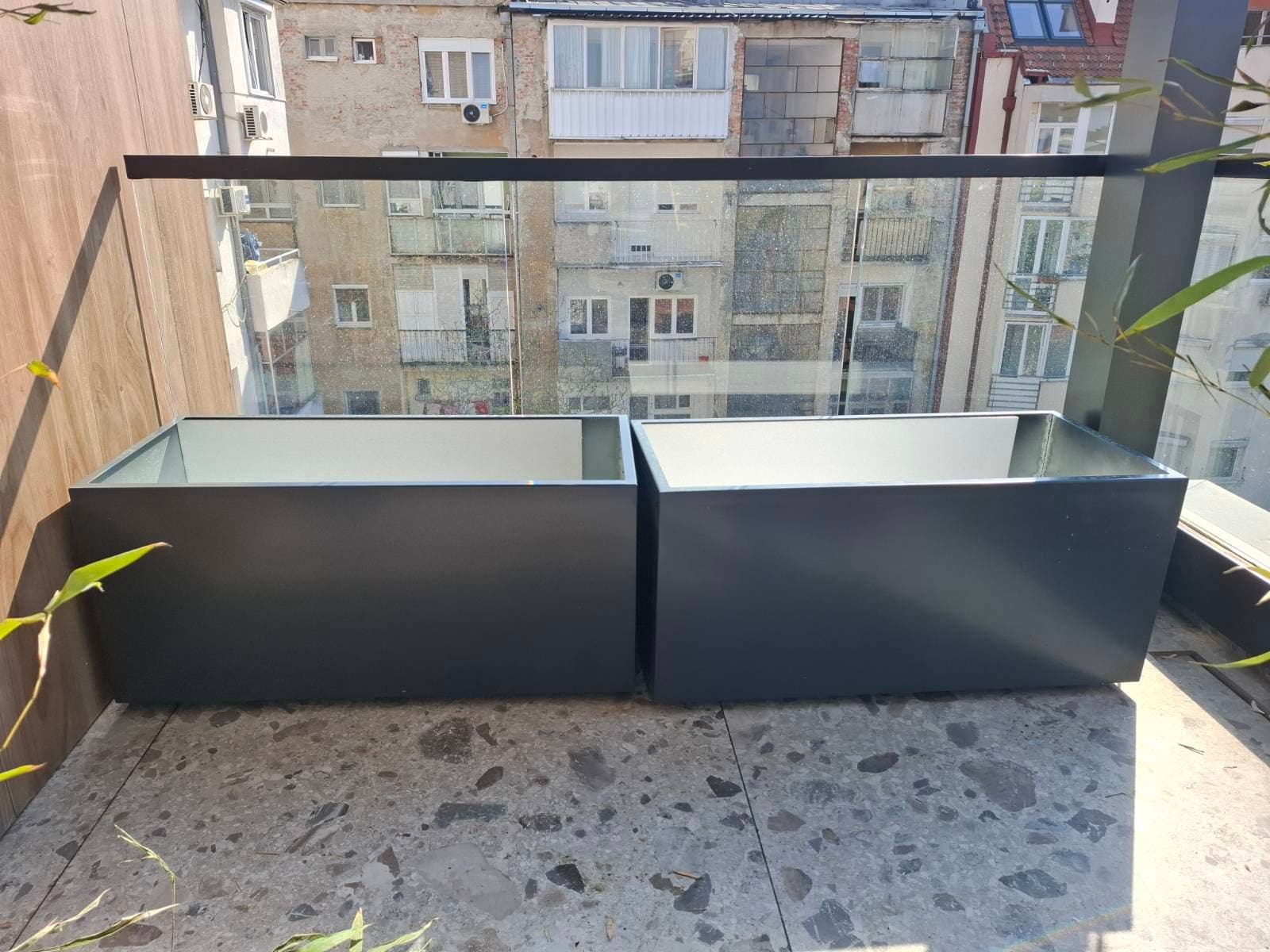 Dve antracit metalne žardinjere na balkonu sa staklenom ogradom